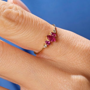 May include: A gold ring with five pink gemstones and a single white gemstone. The ring is on a person's finger.