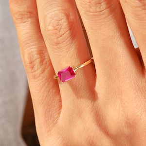 May include: A gold ring with a bright pink rectangular gemstone.