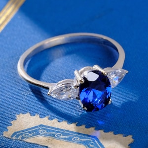 May include: A silver ring with a large blue oval-shaped gemstone surrounded by two smaller pear-shaped clear gemstones.