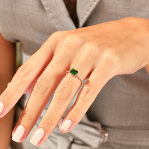 May include: A silver ring with a green emerald-cut gemstone and a row of small clear gemstones around the band.
