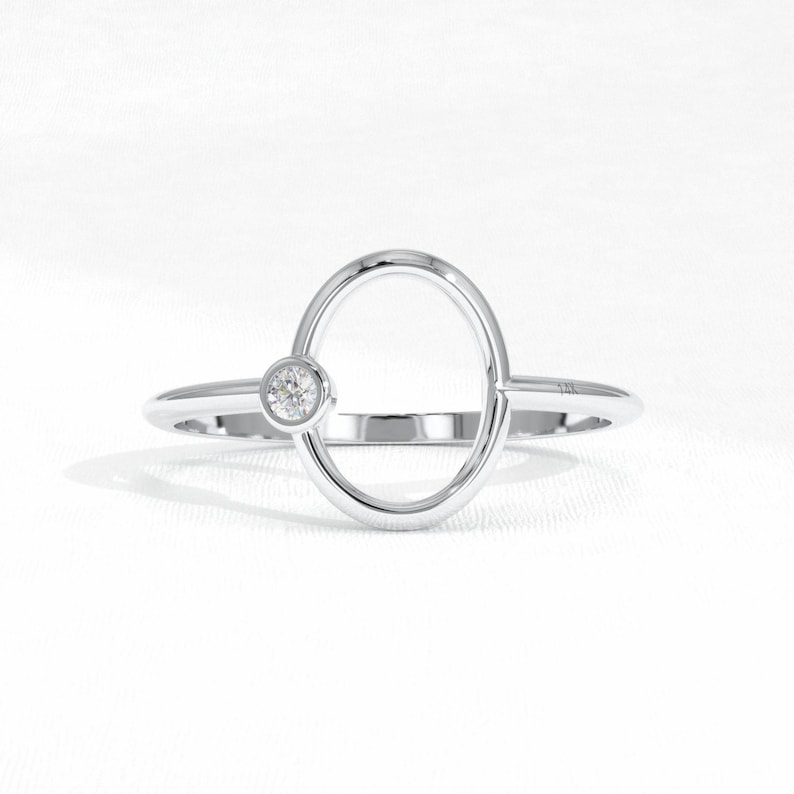 Puede incluir: Anillo de plata con dise&ntilde;o ovalado y una peque&ntilde;a gema redonda y transparente. El anillo tiene una est&eacute;tica minimalista y moderna, sobre un fondo blanco.