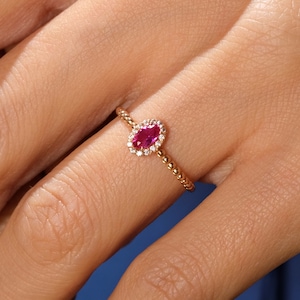 May include: A gold ring with a red oval gemstone surrounded by smaller white gemstones.