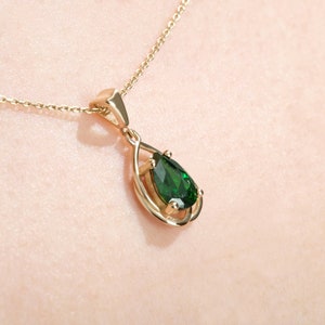 May include: A gold chain necklace with a pear-shaped green gemstone pendant. The pendant is set in a gold frame with a delicate design.