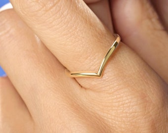 May include: A polished yellow gold ring featuring a V-shaped chevron design. The band has a smooth, rounded profile and a reflective metallic finish, worn on a finger to showcase the pointed silhouette of the jewellery piece.