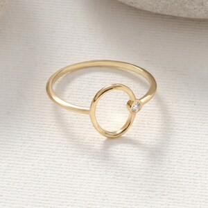 Puede incluir: Un anillo dorado con un dise&ntilde;o ovalado y una peque&ntilde;a gema transparente. El anillo tiene una banda delgada y un estilo minimalista, adecuado para el uso diario. La gema est&aacute; engastada en un engaste de bisel.