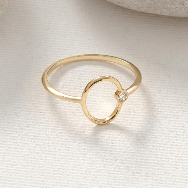 Puede incluir: Un anillo dorado con un dise&ntilde;o ovalado y una peque&ntilde;a gema transparente. El anillo tiene una banda delgada y un estilo minimalista, adecuado para el uso diario. La gema est&aacute; engastada en un engaste de bisel.
