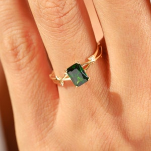 May include: A gold ring featuring a green emerald-cut gemstone and small clear stones on the band.