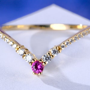 May include: A gold ring with a pink gemstone and clear stones set in a V-shape.