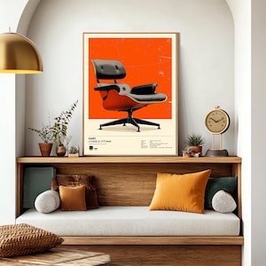May include: A framed poster featuring an Eames Lounge & Ottoman chair against a vibrant orange background. The chair is depicted in black and reddish-brown tones, with a black base. The poster includes the text "EAMES LOUNGE & OTTOMAN".