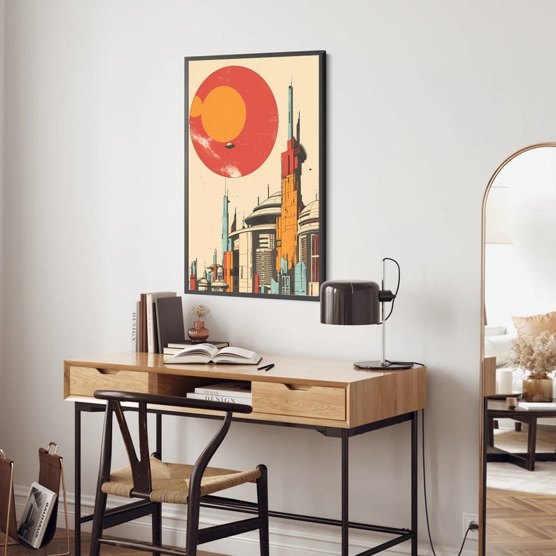 May include: A retro-style poster featuring a cityscape with tall buildings and a large red sun with an orange planet in the background. The poster is framed in black and hanging on a white wall above a wooden desk.