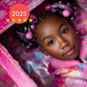 May include: A young person with dark skin and braided hair, adorned with pink and silver accessories, gazes directly at the viewer. The image is dominated by shades of pink, with a pink robe and a pink background. The image includes the text "2025" and "original".