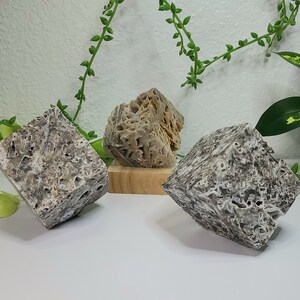 May include: Three gray and brown textured stone cubes. The cubes are arranged on a white surface. The cubes are different sizes and shapes.