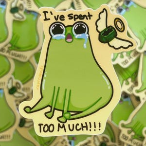 May include: A sticker featuring a cartoon frog with large, tearful eyes and the text "I've spent TOO MUCH!!!". The frog is green with a yellow background and a small halo. The sticker has a whimsical and humorous design.