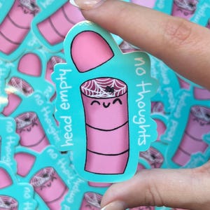 Puede incluir: Una pegatina rosa con un diseño de dibujos animados. La pegatina presenta un cilindro rosa con una telaraña y una araña sonriente. La pegatina tiene las palabras "head empty" y "no thoughts" en un borde turquesa.