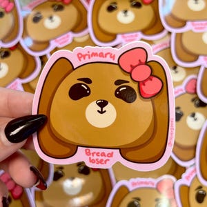 May include: A brown cartoon bear sticker with a pink border and a pink bow. The sticker has the word "Primary" at the top and "Bread loser" at the bottom. The sticker is surrounded by other similar stickers.