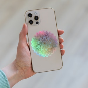 May include: A white iPhone with a gold mandala sticker on the back. The mandala is iridescent and has a rainbow effect.