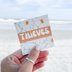 May include: A white sticker with a daisy pattern and the text "THIEVES HOUSEHOLD CLEANER" in orange.