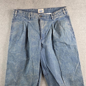 May include: Close-up of blue acid wash Dockers trousers. The trousers have a button and zip closure, belt loops, and pleats at the waist. The Dockers logo is visible on the back of the waistband. The trousers are made of a denim material.