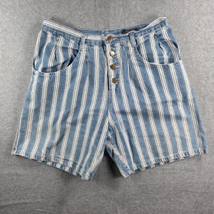 Puede incluir: Shorts vaqueros a rayas verticales azules y blancas, con bragueta de botones y bolsillos delanteros. Estos shorts de cintura alta tienen un estilo clásico. Las rayas crean un efecto adelgazante.