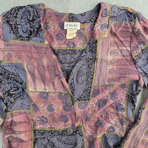 May include: A vintage button-down shirt with a patchwork design. The shirt features a V-neck and is composed of various patterned fabrics in shades of purple, pink, and black. The label reads "ESSAY".