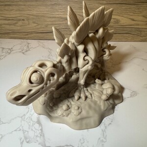 Pu&ograve; includere: Un modello stampato in 3D di uno scheletro di dinosauro con un design dettagliato e articolato. Lo scheletro &egrave; in posa in posizione di camminata con la testa abbassata e la coda sollevata. Il modello &egrave; dipinto in un colore beige chiaro e presenta una superficie testurizzata.