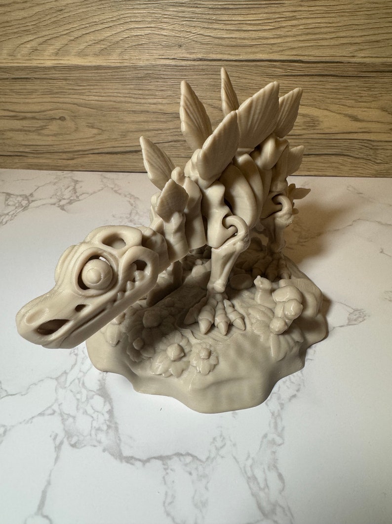 Pu&ograve; includere: Un modello stampato in 3D di uno scheletro di dinosauro con un design dettagliato e articolato. Lo scheletro &egrave; in posa in posizione di camminata con la testa abbassata e la coda sollevata. Il modello &egrave; dipinto in un colore beige chiaro e presenta una superficie testurizzata.