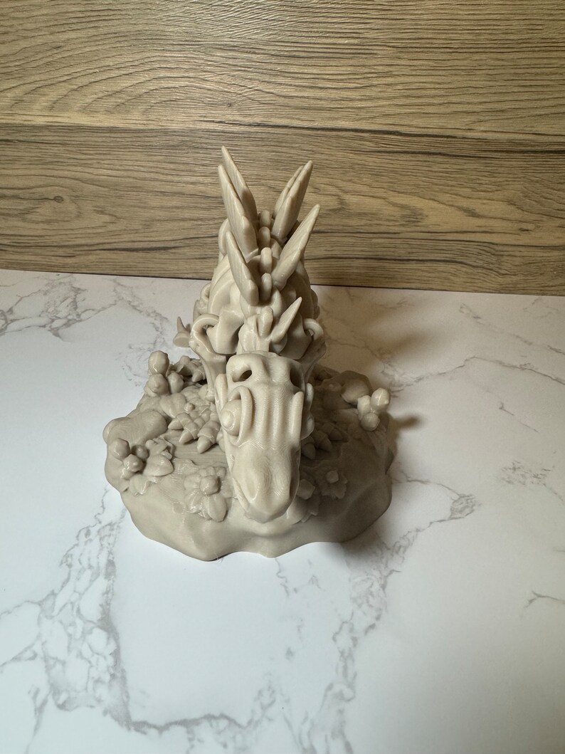 Pu&ograve; includere: Una statuetta di drago grigia stampata in 3D con una schiena spinosa e squame dettagliate. Il drago &egrave; in posa su una base rocciosa con piccole piante.