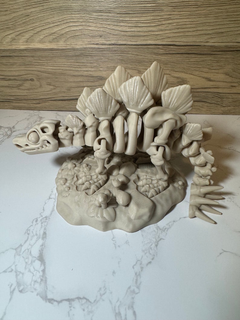 Pu&ograve; includere: Un modello di scheletro di dinosauro in plastica beige con una coda spinosa e una fila di piastre lungo la schiena. Il modello &egrave; posto su una base con una superficie testurizzata.