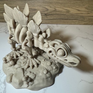 Pu&ograve; includere: Un modello stampato in 3D di uno scheletro di dinosauro con un cranio dettagliato e una schiena spinosa. Il dinosauro &egrave; in posa su una base con una texture rocciosa.