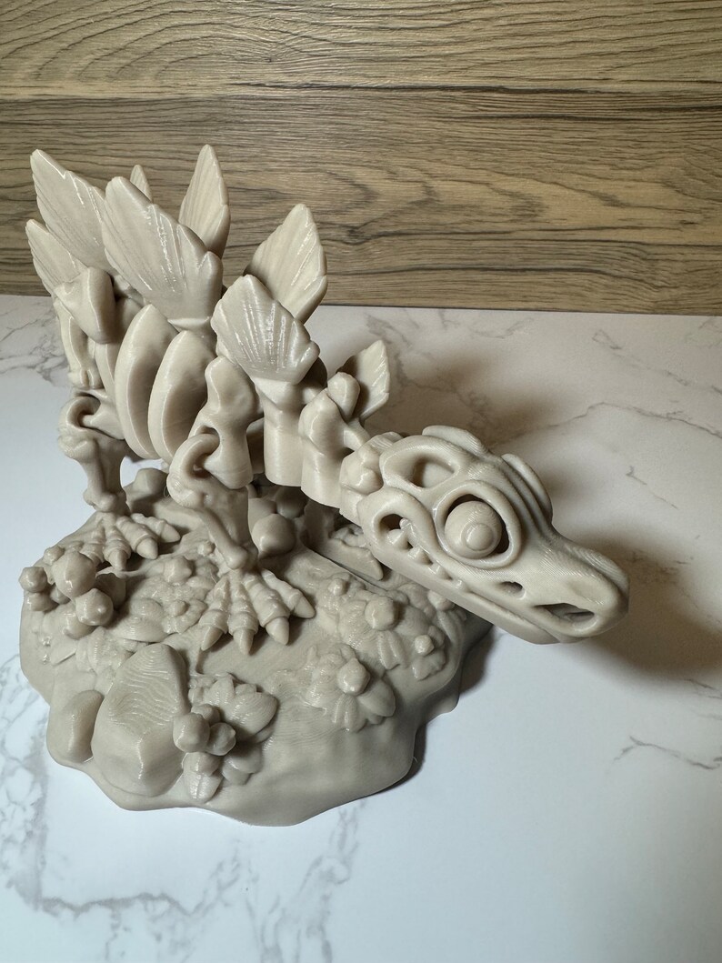 Pu&ograve; includere: Un modello stampato in 3D di uno scheletro di dinosauro con un cranio dettagliato e una schiena spinosa. Il dinosauro &egrave; in posa su una base con una texture rocciosa.