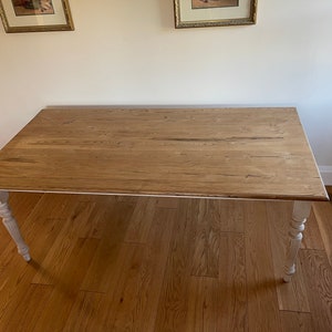 May include: A wooden table with a natural wood top and white painted legs. The table has a simple design and is perfect for a dining room or kitchen.