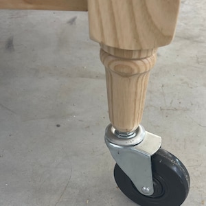 May include: A wooden table leg with a turned design and a black caster wheel.