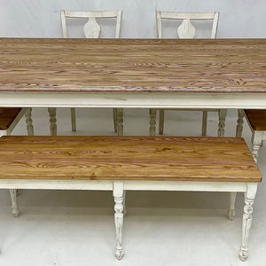 May include: A white farmhouse style dining table with a wood top and four chairs. A matching bench is in front of the table.