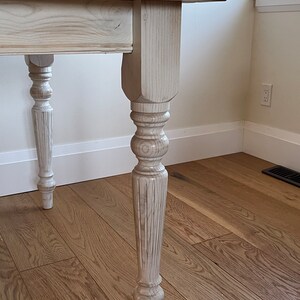 May include: White painted wooden table with a natural wood top and turned legs. The table has a simple, farmhouse style.