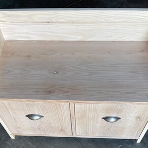 May include: A light wood bench with two doors and two metal handles. The bench has a curved back and a flat top.