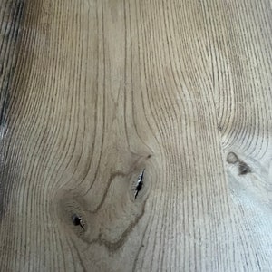May include: Close-up of a light brown wood surface with a natural grain pattern. The wood has a knot with two small holes in it.