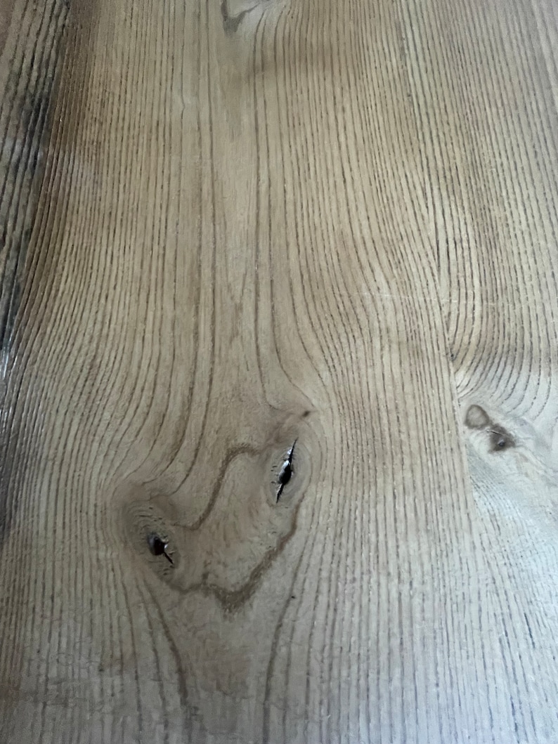 May include: Close-up of a light brown wood surface with a natural grain pattern. The wood has a knot with two small holes in it.