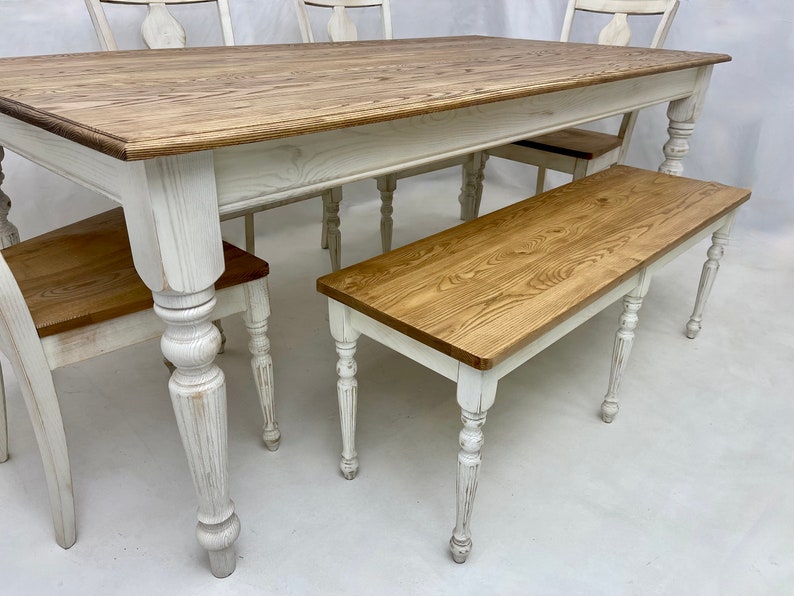 May include: White farmhouse style dining table with a natural wood top and matching bench. The table has turned legs and the bench has turned legs and a natural wood top.