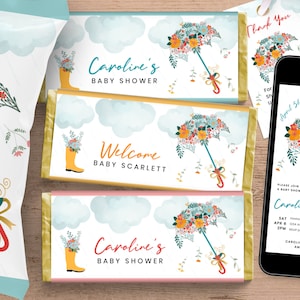May include: A set of three chocolate bar wrappers with a floral umbrella design. The wrappers are decorated with clouds, rainboots, and the text "Caroline's Baby Shower" and "Welcome Baby Scarlett".