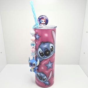 Puede incluir: Un vaso de acero inoxidable rosa con un dise&ntilde;o de personaje de dibujos animados azul. El vaso tiene una pajita azul y un amuleto con cuentas y un personaje de dibujos animados azul. El vaso tiene el texto "Salgado's Crafts" en la parte superior.