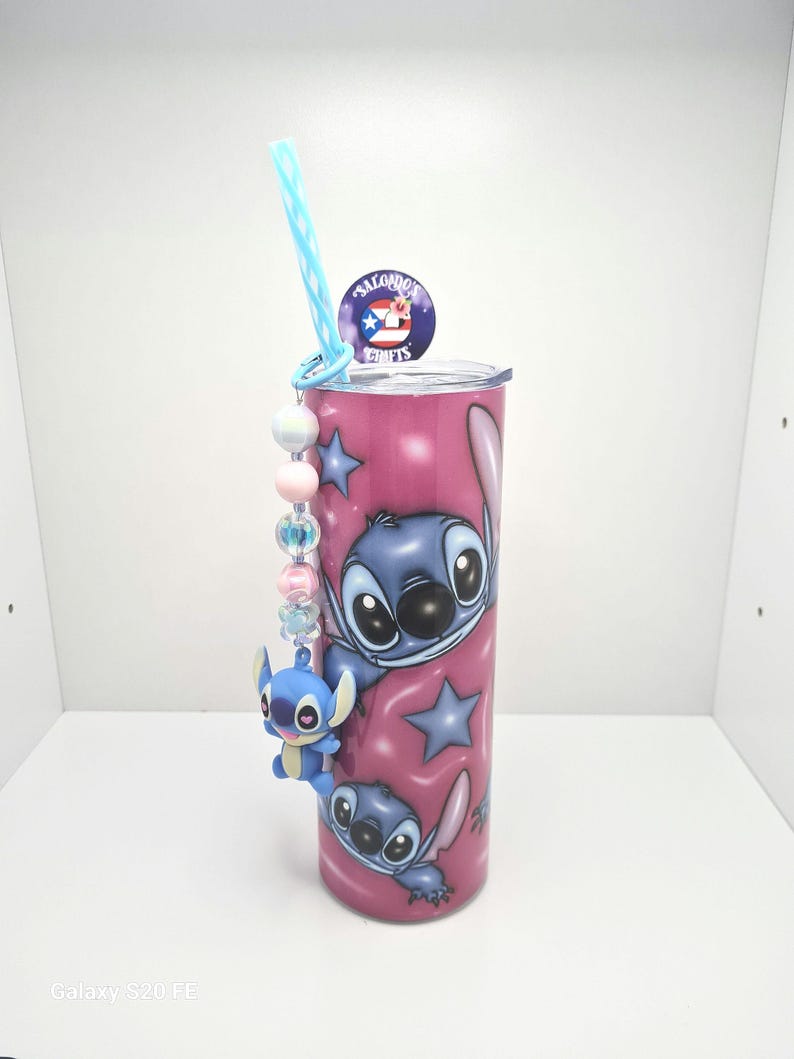 Puede incluir: Un vaso de acero inoxidable rosa con un dise&ntilde;o de personaje de dibujos animados azul. El vaso tiene una pajita azul y un amuleto con cuentas y un personaje de dibujos animados azul. El vaso tiene el texto "Salgado's Crafts" en la parte superior.