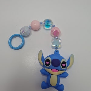 Puede incluir: Un llavero con un dije azul de Stitch, el personaje de Disney, con corazones rosas para los ojos. El llavero est&aacute; hecho de cuentas azules, rosas y blancas iridiscentes. Tiene un anillo de metal azul.