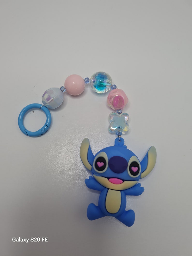 Puede incluir: Un llavero con un dije azul de Stitch, el personaje de Disney, con corazones rosas para los ojos. El llavero est&aacute; hecho de cuentas azules, rosas y blancas iridiscentes. Tiene un anillo de metal azul.
