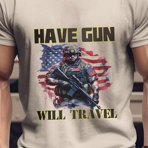 Peut inclure: T-shirt beige clair avec l'inscription dorée "HAVE GUN WILL TRAVEL". Le t-shirt présente un graphisme d'un soldat tenant un fusil devant un drapeau américain.