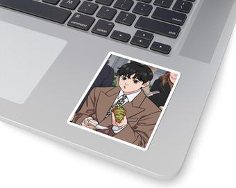 May include: A sticker featuring an anime-style illustration of a person in a brown suit and patterned tie, holding a sandwich and a small dessert. The sticker is placed on a laptop.
