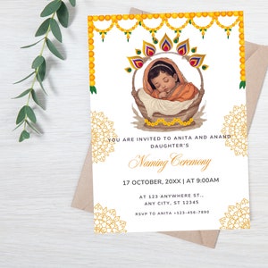 May include: A white invitation card with gold accents and a floral design. The card announces a Naming Ceremony for a baby girl. The text reads "You are invited to Anita and Anand's daughter's Naming Ceremony. 17 October, 20XX | At 9:00 AM. At 123 Anywhere St., Any City, ST 12345. RSVP to Anita +123-456-7890."