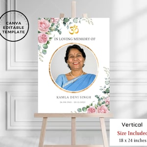 Pode incluir: Um cartaz comemorativo branco com uma borda floral e uma foto de uma mulher com um sari azul. O cartaz diz "In Loving Memory of Kamla Devi Singh 26.08.1942 - 20.12.2025" e apresenta um símbolo Om dourado. O cartaz mede 46 x 61 cm.