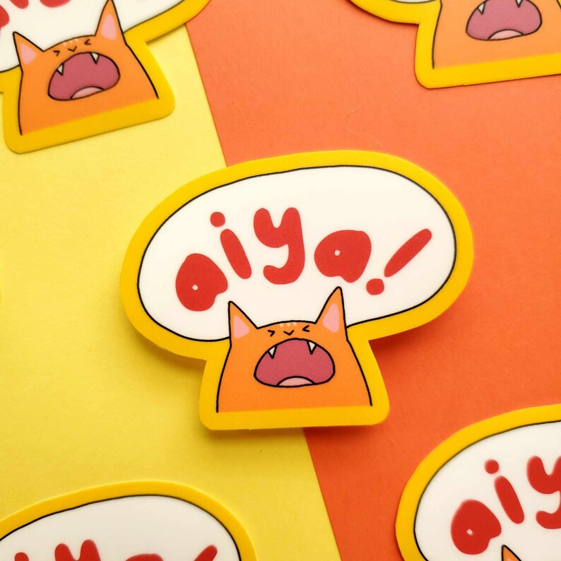May include: Orange and yellow sticker featuring a cartoon cat shouting "aiya!" in a speech bubble.