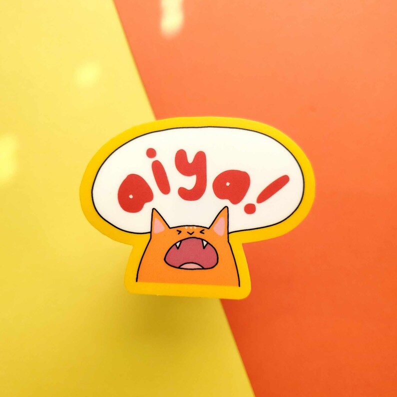 May include: A yellow and orange sticker with a cartoon cat yelling "aiya!" in a speech bubble.