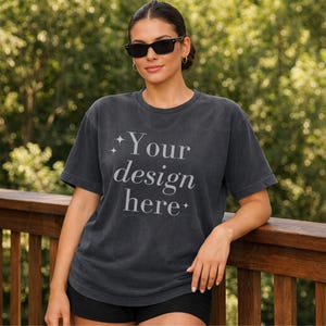May include: Dark gray t-shirt with the text "Your design here" in a stylized font. The shirt has a vintage, washed appearance. The model is wearing black sunglasses and black shorts.